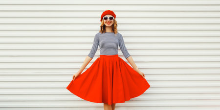 Portrait of beautiful happy smiling young woman model posing in red skirt, french beret, heart shaped sunglasses on white backgroundの写真素材