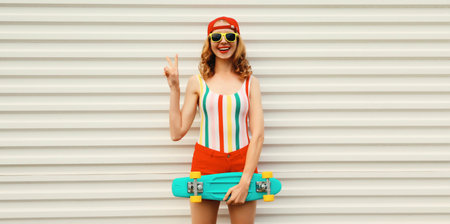 Summer portrait of happy cheerful stylish young woman with skateboard in colorful clothes posing on white backgroundの写真素材