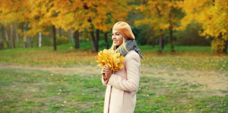 Beautiful happy smiling young woman holding yellow maple leaves looking away wearing a french beret...