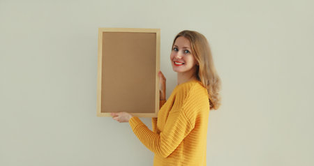 Happy smiling young woman decorating interior, hanging blank photo frame, wooden picture, artwork...