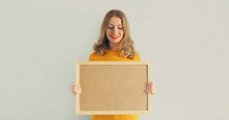 Happy smiling young woman decorating interior, hanging blank photo frame, wooden picture, artwork...