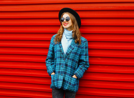 Fashion pretty woman wearing a black hat coat jacket over colorful red backgroundの写真素材
