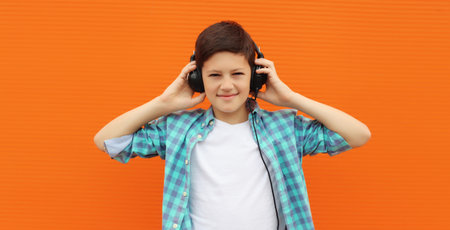 Portrait of happy modern teenage boy listening to music with headphones in the city on orange wall...