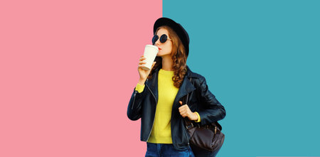 Stylish young woman holding cup of coffee drink in black hat, leather jacket with backpack on...