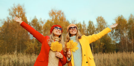 Happy young two women friends with yellow leaves in autumn park enjoying warm weather, stylish...