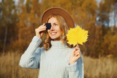 Portrait of stylish happy young woman holding plastic credit bank card with yellow leaves in autumn...