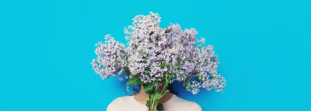 Portrait of woman covering her head with bouquet of fresh lilac flowers on blue background