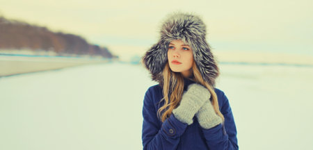 Portrait of beautiful blonde young woman posing in winter hat outdoors in park