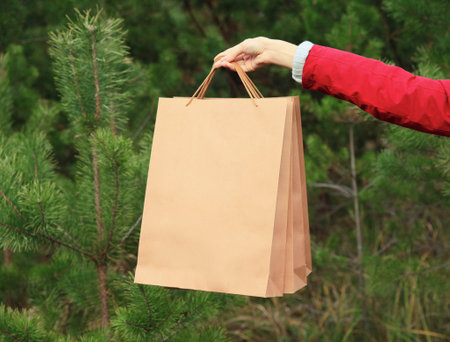 Purchase, holidays, female hand holding showing paper shopping bags, gift against christmas tree backgroundの写真素材