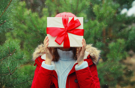 Close up woman holding festive red gift box in her hands in winter forest on Christmas tree...