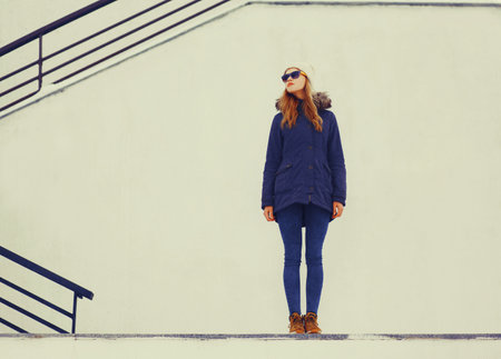 Fashion pretty blonde woman wearing jacket and hat posing in winter city over white wall backgroundの写真素材