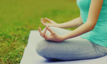 Young woman doing yoga exercises on a mat on the grass in summer parkの写真素材