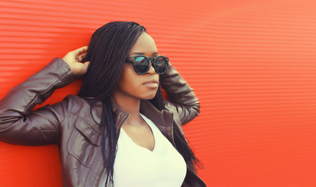 Fashionable portrait of young African woman in casual clothing, stylish modern black girl in glasses with dreadlocks posing in the city on red backgroundの写真素材