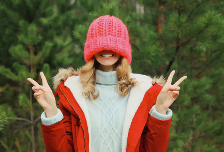 Happy smiling young woman having fun enjoys snow, warm weather in winter park against Christmas...