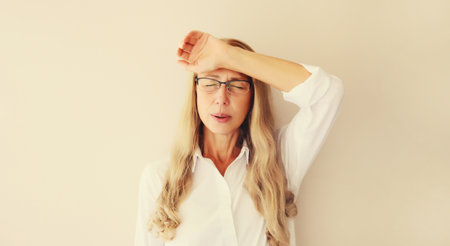 Exhausted tired caucasian mature woman employee with headache, stress, fatigue, temples pain, suffers from migraine, tension in the head in the officeの写真素材