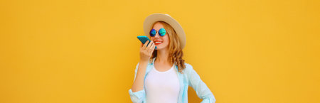 Happy young woman holding talking on the phone, using voice command recorder, assistant or takes calling on smartphone in casual clothing on bright yellow backgroundの写真素材