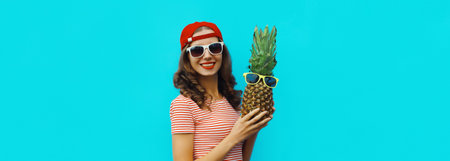 Summer vacation, happy joyful young woman with pineapple in glasses, cheerful girl with fruits posing on blue studio backgroundの写真素材