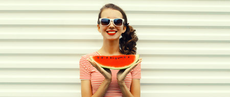 Summer portrait of happy young woman eating fresh slice of watermelon in glasses on white backgroundの写真素材