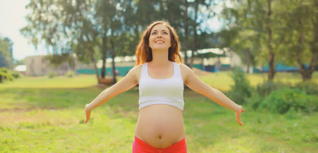 Maternity, pregnancy, happy young pregnant woman with big belly enjoying warm sunny day in summer parkの写真素材