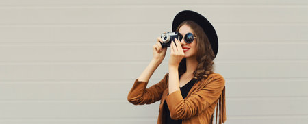 Portrait of beautiful happy young woman photographer taking picture with camera, stylish creative girl in black hat on gray backgroundの写真素材
