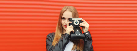 Portrait of stylish young woman photographer with film camera, modern girl taking a picture standing on red backgroundの写真素材