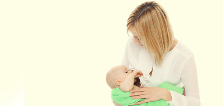 Happy young mother breastfeeding her baby on white studio backgroundの写真素材