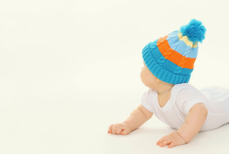 Happy cute baby in knitted hat crawling on the floor playing on white studio backgroundの写真素材