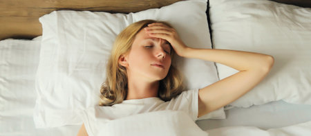 Exhausted tired woman touching head, suffering from headache, stress, fatigue, temples pain, migraine, loud noise, tension lying on the pillow in bed in bedroom at homeの写真素材