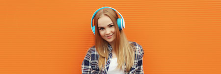 Summer portrait of happy modern young woman listening to music with headphones on orange wall backgroundの写真素材