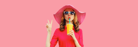 Summer portrait of beautiful young woman drinking fresh juice wearing straw hat, pink dress on studio backgroundの写真素材
