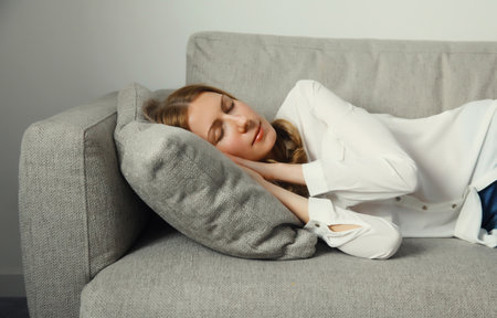Happy relaxed young woman sleeping lying on the couch on gray soft comfortable pillow in living room at homeの写真素材