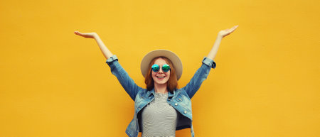 Summer holidays, inspired happy cheerful smiling young woman raising her hands up wearing denim clothing, straw hat on colorful yellow backgroundの写真素材
