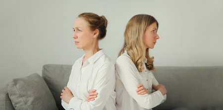 Upset offended caucasian two women, mature mother or sister and adult daughter crying together sitting on couch at homeの写真素材