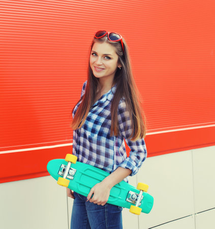 Summer portrait of happy cheerful stylish young woman with skateboard, teenager girl in casual clothes, glasses posing on red backgroundの写真素材