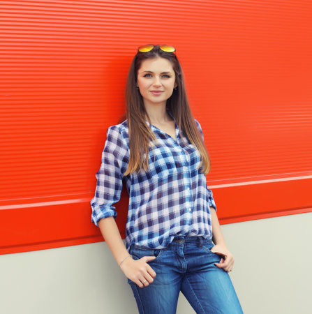Portrait of beautiful smiling brunette young woman with glasses in casual clothing posing on colorful red wall backgroundの写真素材