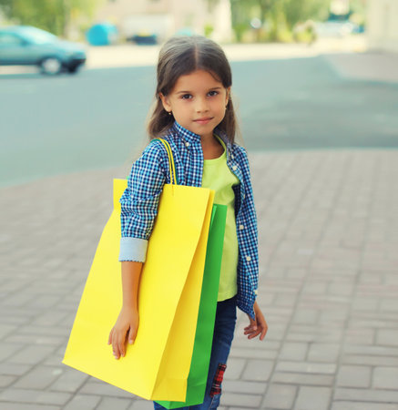 Little girl child with colorful shopping bags posing on city streetの写真素材
