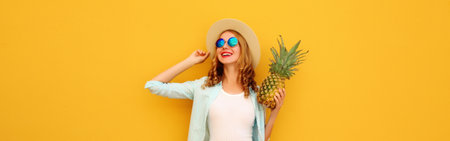 Summer vacation, happy joyful young woman with pineapple fruit in tourist hat, cheerful girl posing on yellow studio backgroundの写真素材