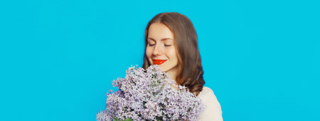 Portrait of beautiful happy smiling woman with bouquet of fresh lilac flowers, wildflowers on blue backgroundの写真素材