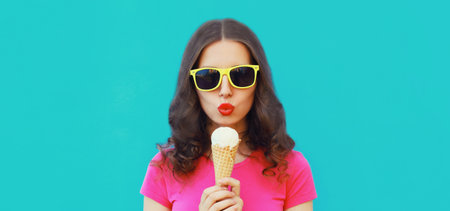 Summer portrait of happy young woman eating ice cream wearing sunglasses on blue backgroundの写真素材