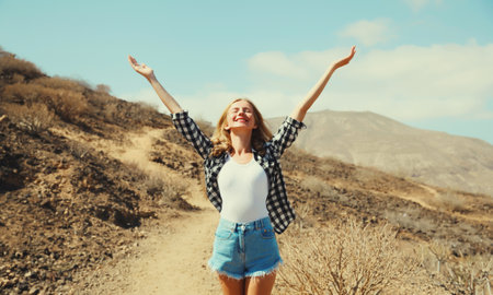 Happy cheerful young woman raising her hands up on hiking trail on top of the mountain, Tenerife, Canary Islands, Spainの写真素材