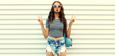 Portrait of stylish modern young woman, cool girl posing wearing shorts, sunglasses on white wall backgroundの写真素材