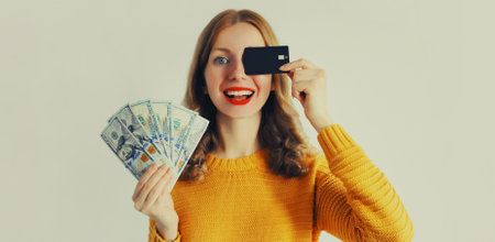 Portrait of happy smiling young woman holding plastic credit bank card and cash money in dollar billsの写真素材