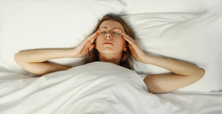Exhausted tired woman touching head, suffering from headache, stress, fatigue, temples pain, migraine, loud noise, tension lying on the bed in bedroom at homeの写真素材