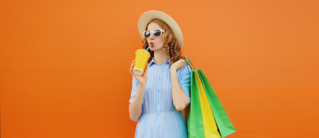 Fashion, shopping and clothing, beautiful relaxed young woman with colorful shopping bags and cup drinking juice in summer tourist hat on bright orange wall backgroundの写真素材