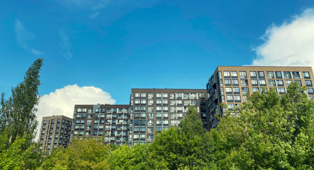Architecture and real estate, residential apartment building with large panoramic windows, modern complex, surrounded by nature, park, green trees, blue sky backgroundの写真素材