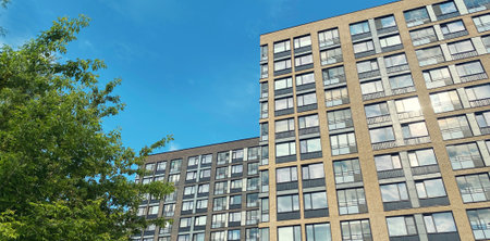 Architecture and real estate, residential apartment building with large panoramic windows, modern complex, surrounded by nature, park, green trees, blue sky backgroundの写真素材