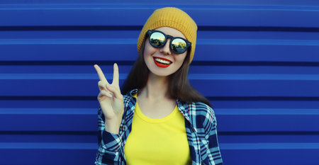 Stylish happy smiling young woman standing in yellow hat with sunglasses, modern cheerful teenage girl posing on vivid wall background in the cityの写真素材