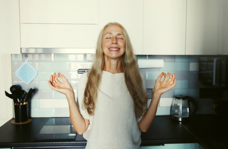 Happy relaxed satisfied woman enjoying with closed eyes at home standing in kitchenの写真素材