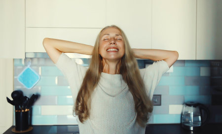 Happy relaxed satisfied woman enjoying with closed eyes at home standing in kitchenの写真素材