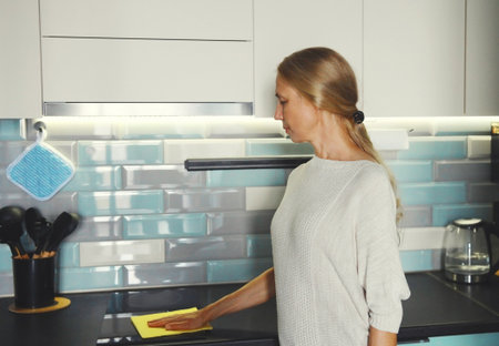 House cleaning concept - woman holding dry microfiber rag wiping the glass surface induction cooker and kitchen countertop from dustの写真素材